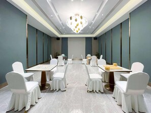 Un salón de conferencias con candelabro, sillas blancas y mesas dispuestas para reuniones.
