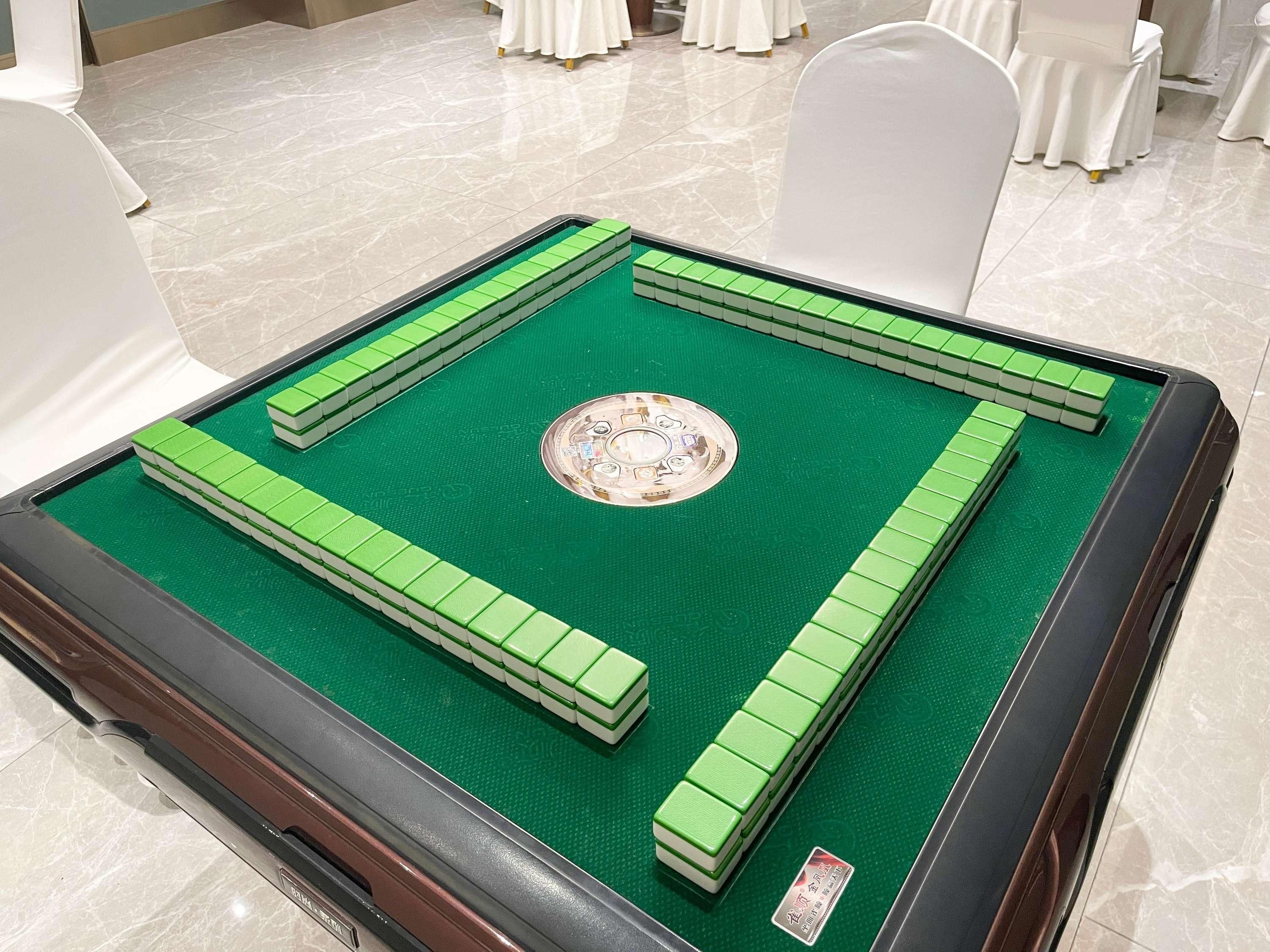 Une table de billard verte, dotée d’un centre circulaire et de bandes périphériques, est placée dans une pièce où se trouvent des chaises blanches et un sol carrelé.