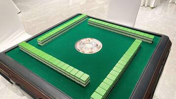 Une table de billard verte, dotée d’un centre circulaire et de bandes périphériques, est placée dans une pièce où se trouvent des chaises blanches et un sol carrelé.