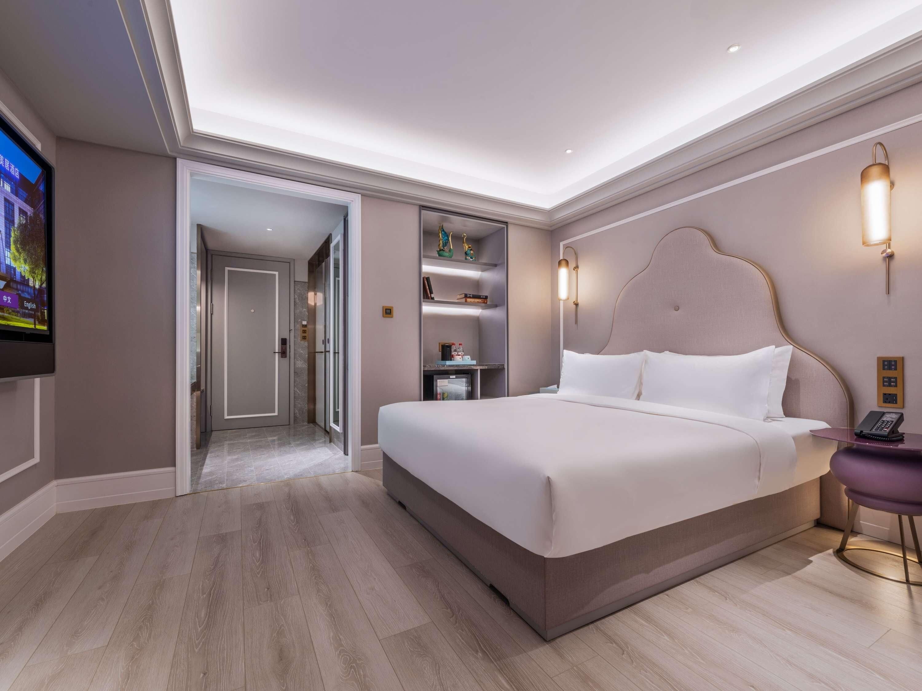 Quarto de hotel moderno com uma cama grande, televisão, escrivaninha com telefone e estante de livros.