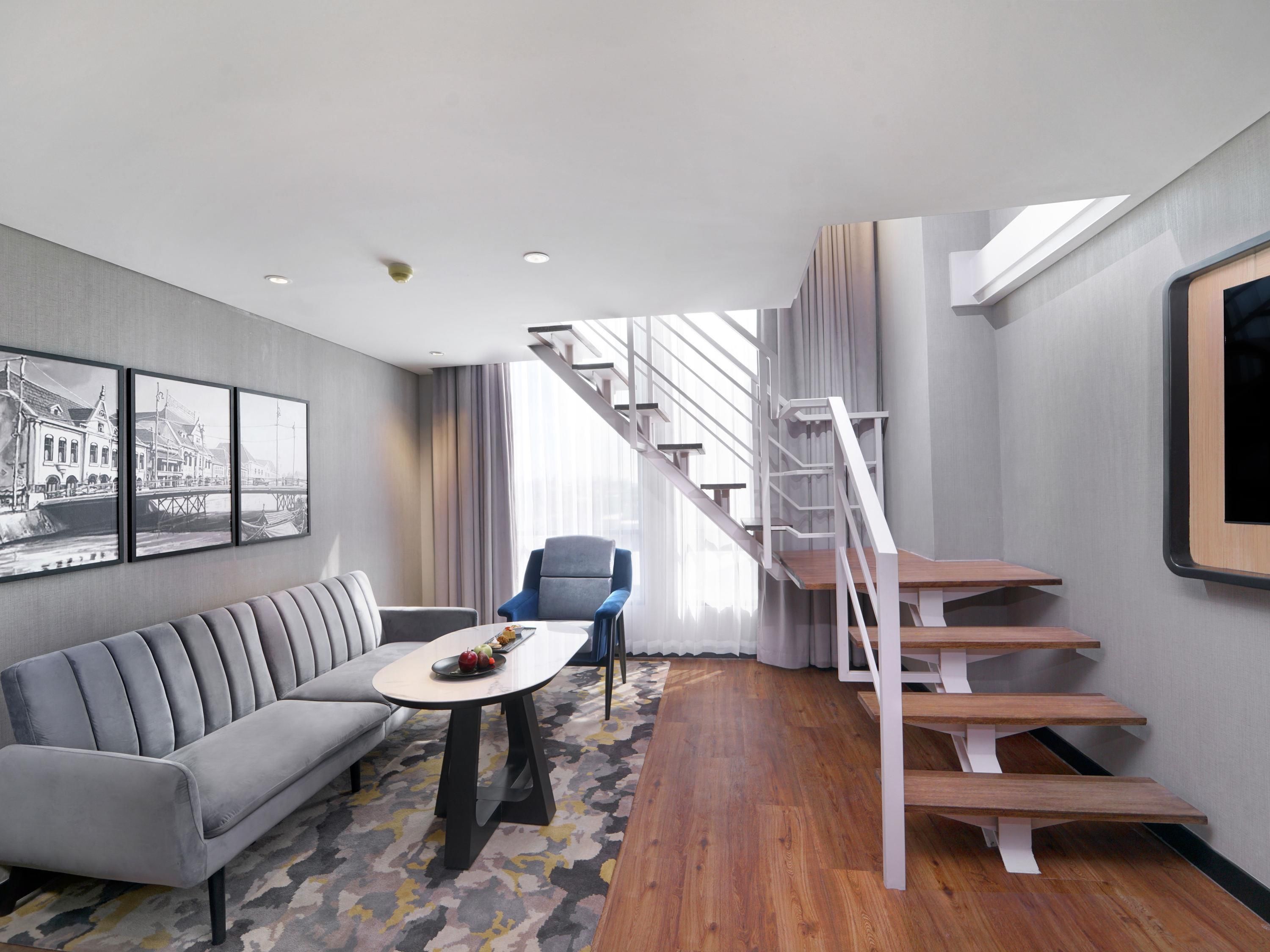 A modern living room with a sofa, a coffee table, a chair, a staircase, and a large window.