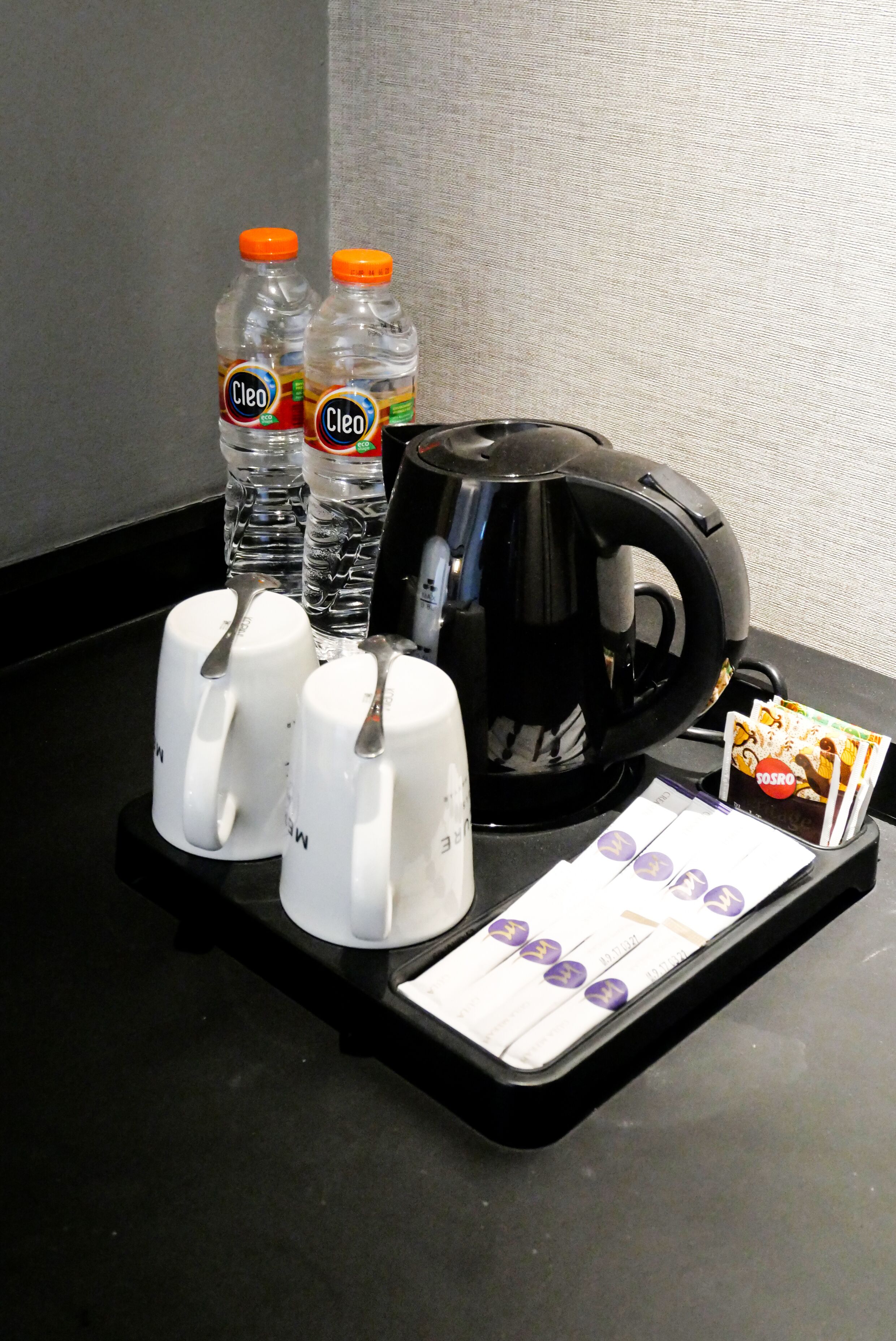 A coffee station with a coffee maker, two water bottles, and a tray with coffee mugs and a card game.