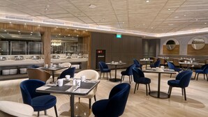 A modern dining area with round tables and blue chairs, a visible exit sign, and a 'HYDRANT' sign. - Mercure Surabaya Manyar (Surabaya)