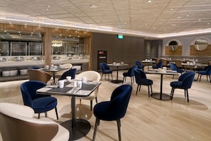 A modern dining area with round tables and blue chairs, a visible exit sign, and a 'HYDRANT' sign. - Mercure Surabaya Manyar (Surabaya)