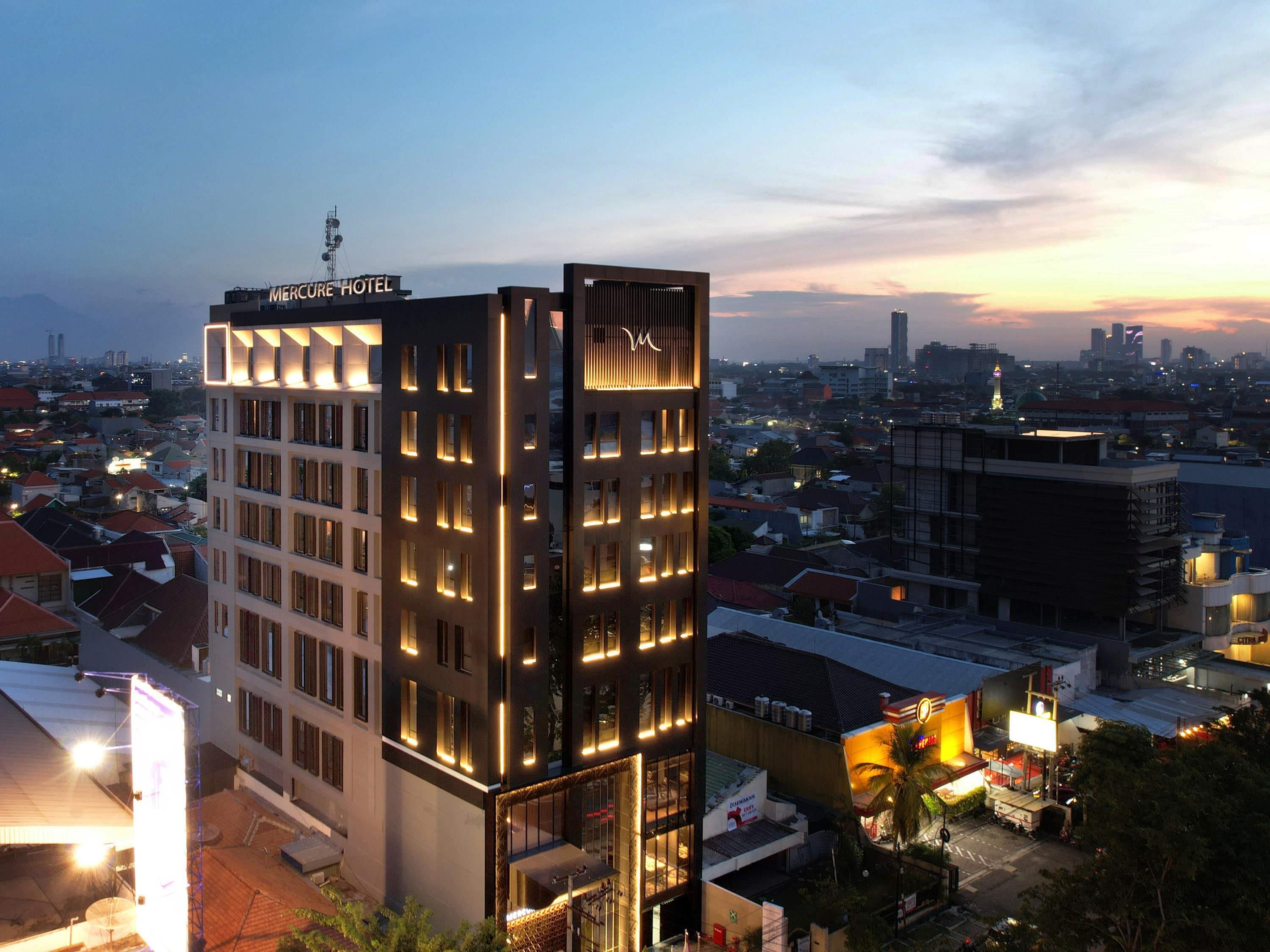A modern hotel with a prominent sign, multiple floors, and a view of the surrounding cityscape at dusk.
