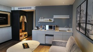Quarto de hotel moderno com cozinha compacta, área de estar com mesa de mármore e guarda-roupa com roupão.