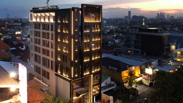A modern hotel with a prominent sign, multiple floors, and a view of the surrounding cityscape at dusk. - Mercure Surabaya Manyar (Surabaya)