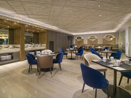 Ein modernes Restaurant mit Marmorböden, blauen und beigen Stühlen und einem zentralen Essbereich mit runden Tischen.