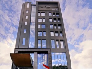 A tall building with a modern architectural design, featuring a series of rectangular windows and a prominent entrance at the base. - Mercure Surabaya Manyar (Surabaya)