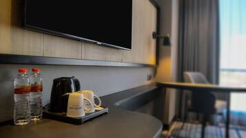 Habitación de hotel con televisión de pantalla plana en la pared, cafetera, dos botellas de agua y una bandeja con taza y control remoto.