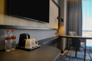 A hotel room with a flat-screen TV mounted on the wall, a coffee maker, two bottles of water, and a tray with a mug and a remote control. - Mercure Surabaya Manyar (Surabaya)