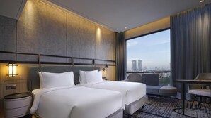 A hotel room with two beds, a seating area, a view of the city, and a large window. - Mercure Surabaya Manyar (Surabaya)