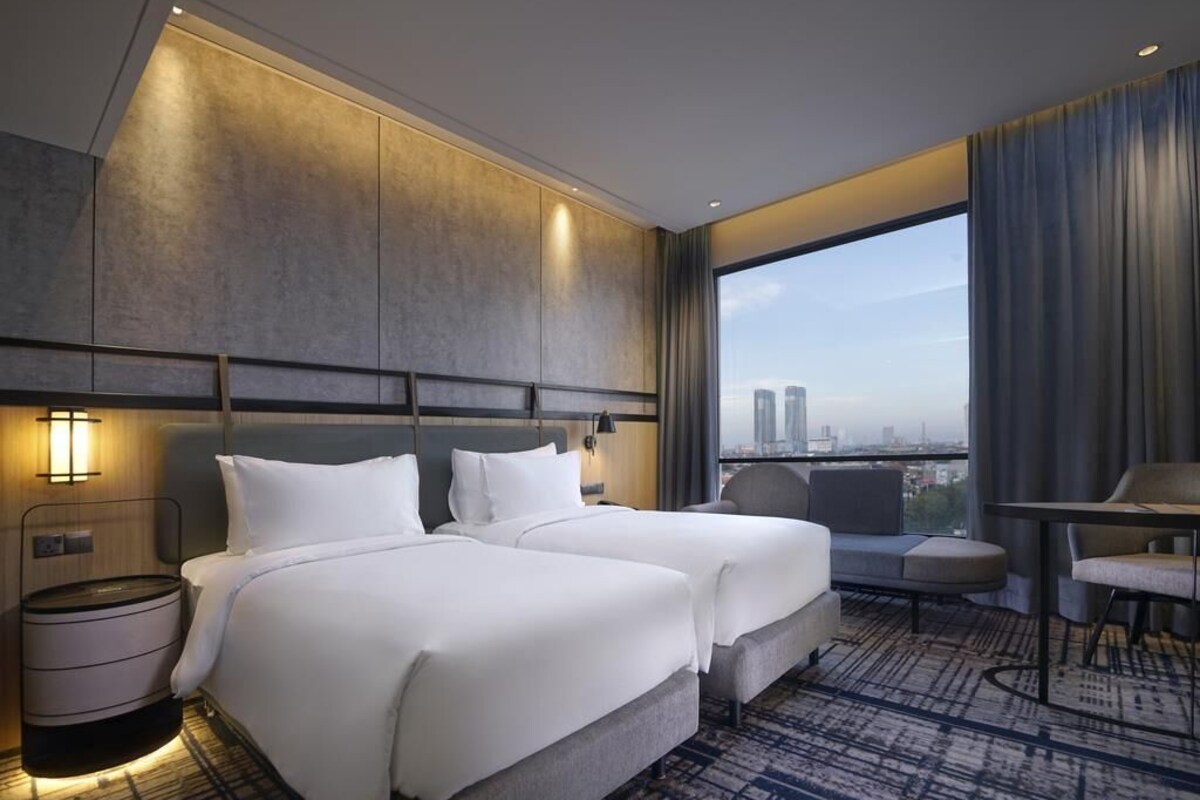 A hotel room with two beds, a seating area, a view of the city, and a large window.