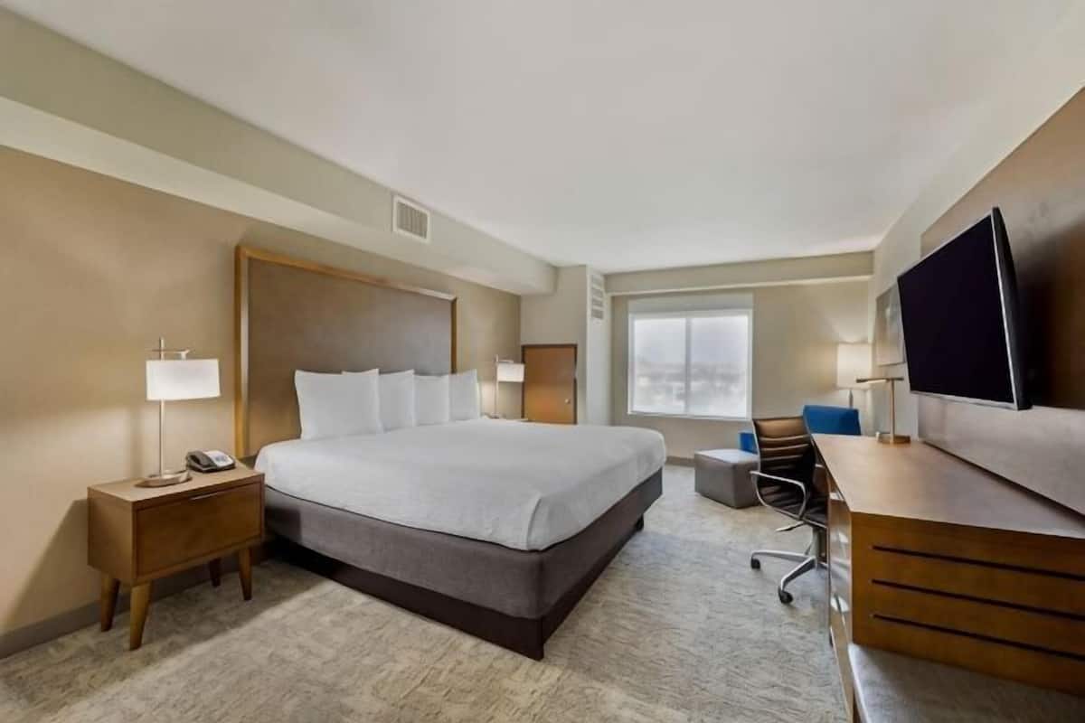 A hotel room with a large bed, bedside tables, a desk, a chair, a TV, and a window.
