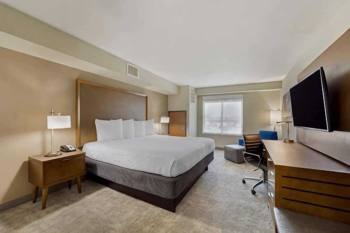 A hotel room with a large bed, bedside tables, a desk, and a television.