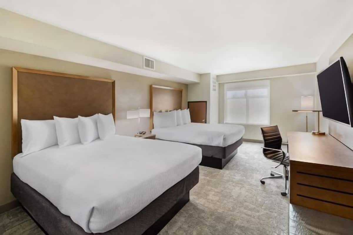 A hotel room with two beds, a desk, a chair, a television, and a window.