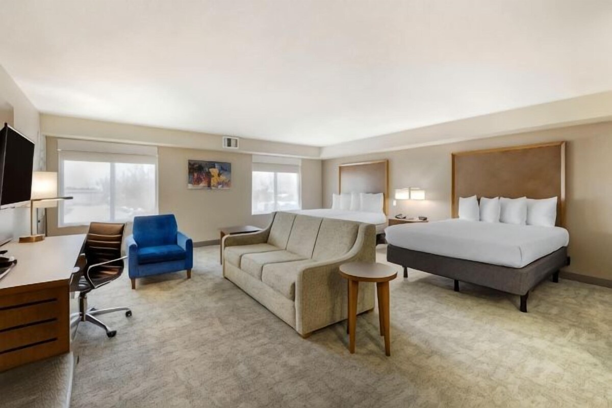 A hotel room with a bed, a desk, a chair, a sofa, and a small table.