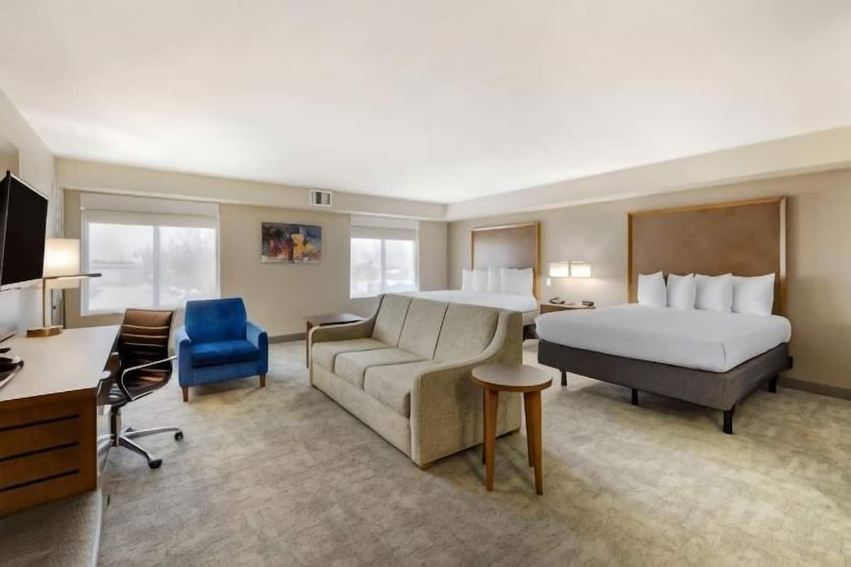 A hotel room with a bed, a desk, a chair, a sofa, and a small table.