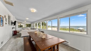 Una habitación amplia con una gran mesa de madera, un sofá blanco y vistas a la playa a través de amplios ventanales.