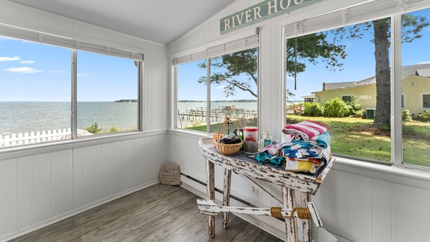 Una habitación con vistas al agua y al muelle, una mesa con varios objetos, y un letrero que dice "RIVER HOUSE".