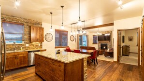 A spacious kitchen with granite countertops, wooden cabinets, and a large island. There is a dining area with a fireplace and a TV mounted on the wall.