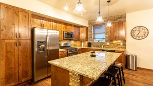 A modern kitchen with wooden cabinets, stainless steel appliances, granite countertops, and pendant lighting.