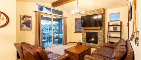 A living room with a fireplace, leather sofas, a coffee table, and a TV mounted on the wall.