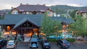 A lodge with a large parking area, a pool, and a mountainous backdrop.