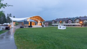 A modern building with a curved roof and a covered outdoor area, surrounded by a well-maintained lawn and residential buildings in the background.