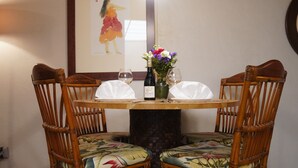 A round wooden table with two chairs, each with a floral cushion. A bottle of wine and two glasses are on the table. - Upgraded Makaha remote work and surf oceanfront condo (Waianae)