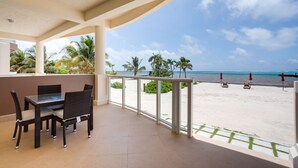 Ein Balkon mit Blick auf einen Strand, ausgestattet mit einem Tisch und Stühlen sowie einem Geländer.