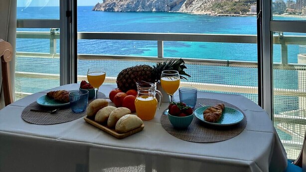 Une table dressée avec des aliments pour le petit-déjeuner, offrant une vue pittoresque sur une île rocheuse et la mer.
