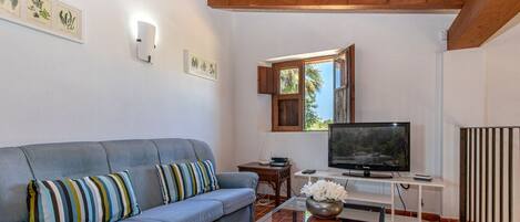 A living room with a sofa, a TV, a small table with a vase, and framed botanical prints on the wall.