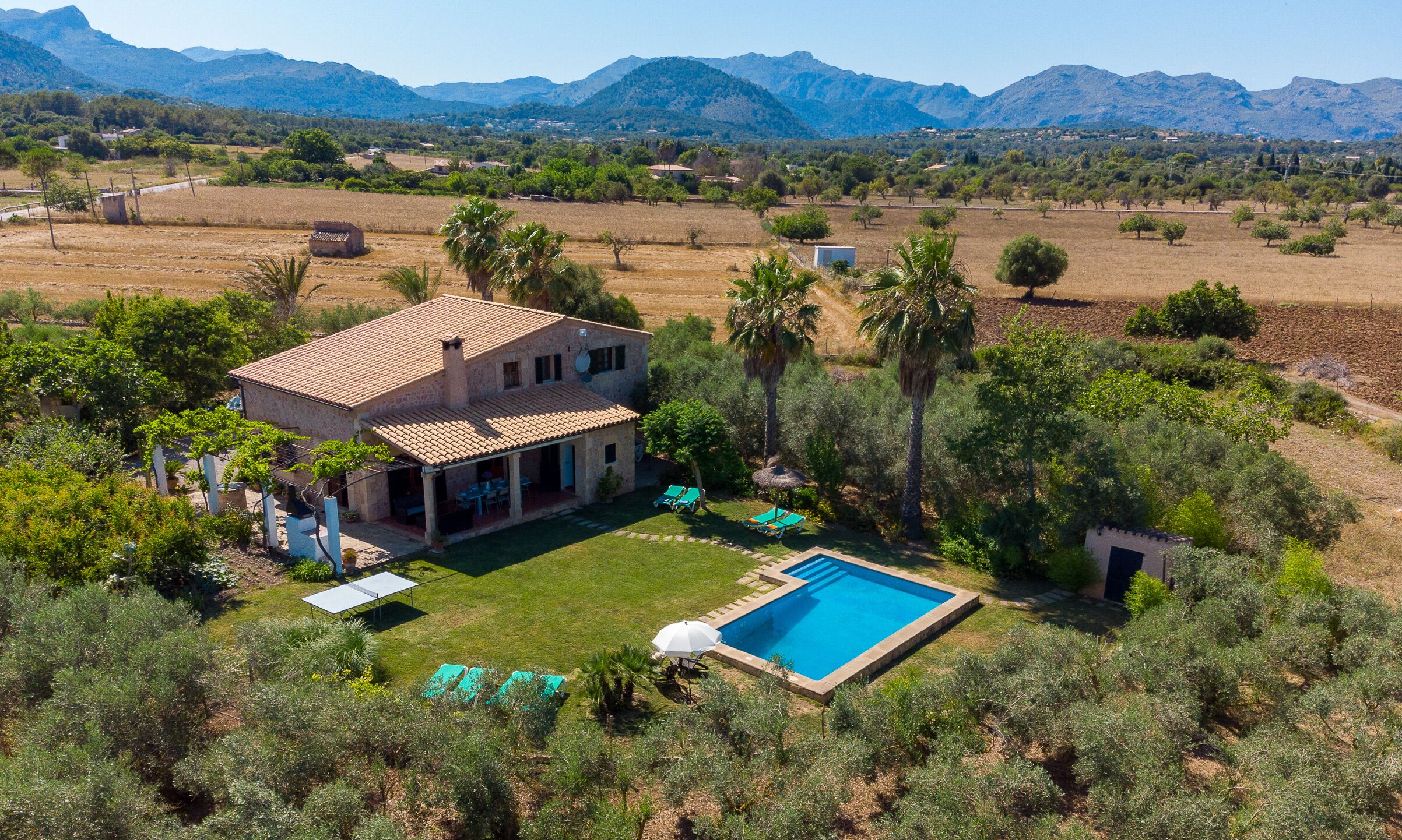 A house with a swimming pool, surrounded by greenery and mountains.