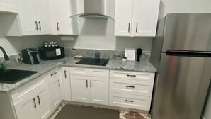 Una cocina con armarios blancos, un refrigerador de acero inoxidable, una cafetera y baldosas de piso estampadas.