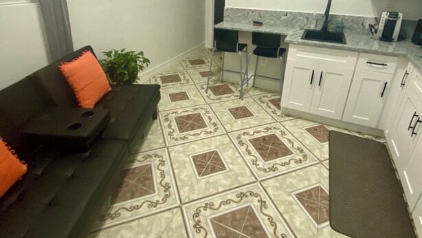 Un espacio habitable compacto con sofá, una pequeña cocina y piso de baldosas.