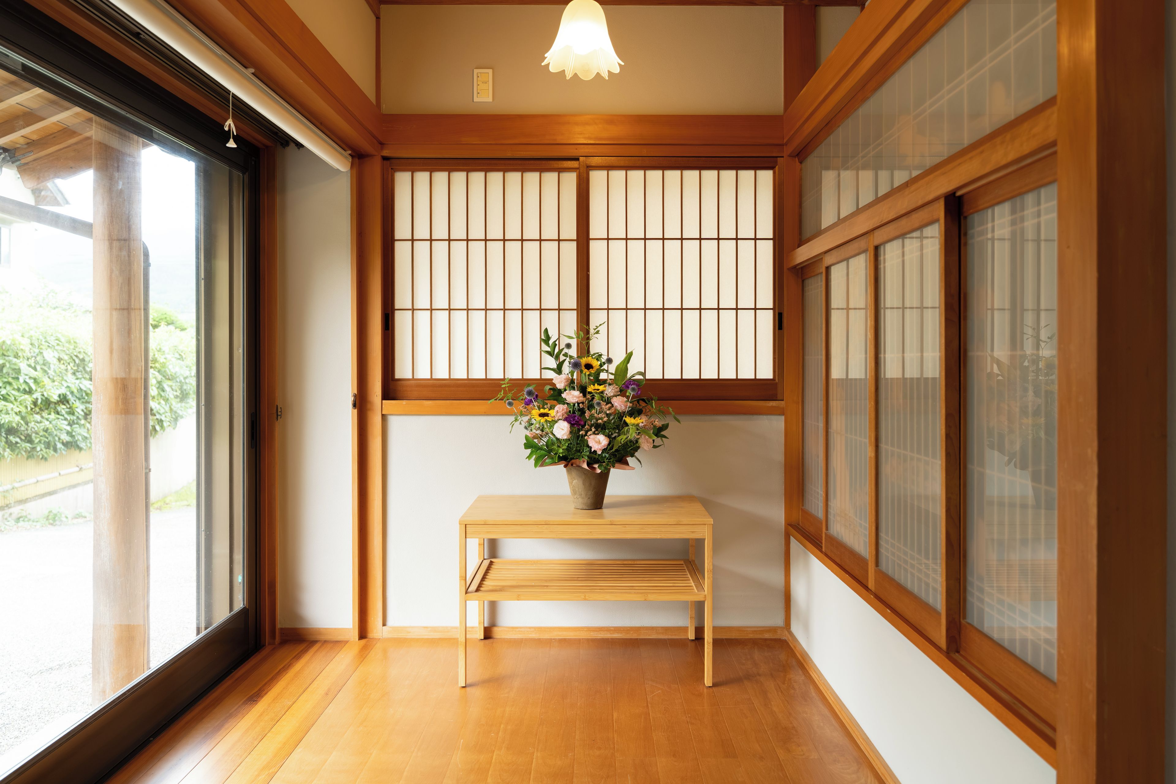Una habitación tradicional japonesa con suelo de tatami, un banco de madera y un jarrón de flores.