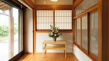 Una habitación tradicional japonesa con suelo de tatami, un banco de madera y un jarrón de flores.