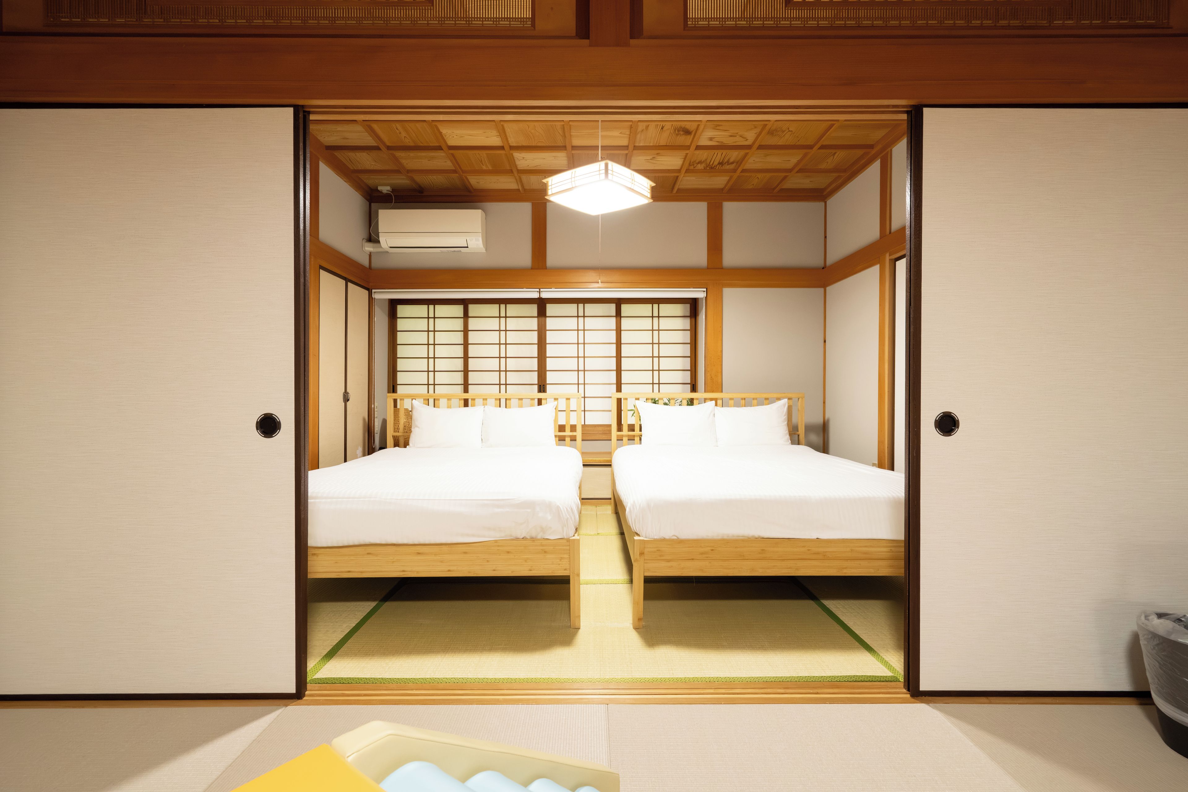A traditional Japanese-style room with two wooden beds, tatami mats, sliding doors, and a shoji screen.