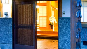 Un ingresso tradizionale giapponese con una porta scorrevole, un'orchidea in vaso e un pavimento piastrellato.