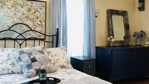 Une chambre à coucher comprenant un lit, un ventilateur de plafond, une fenêtre avec des rideaux, une commode et un miroir.
