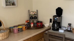 Une cuisine équipée d’une machine à café, de tasses, de bocaux et d’une étagère remplie d’objets divers.
