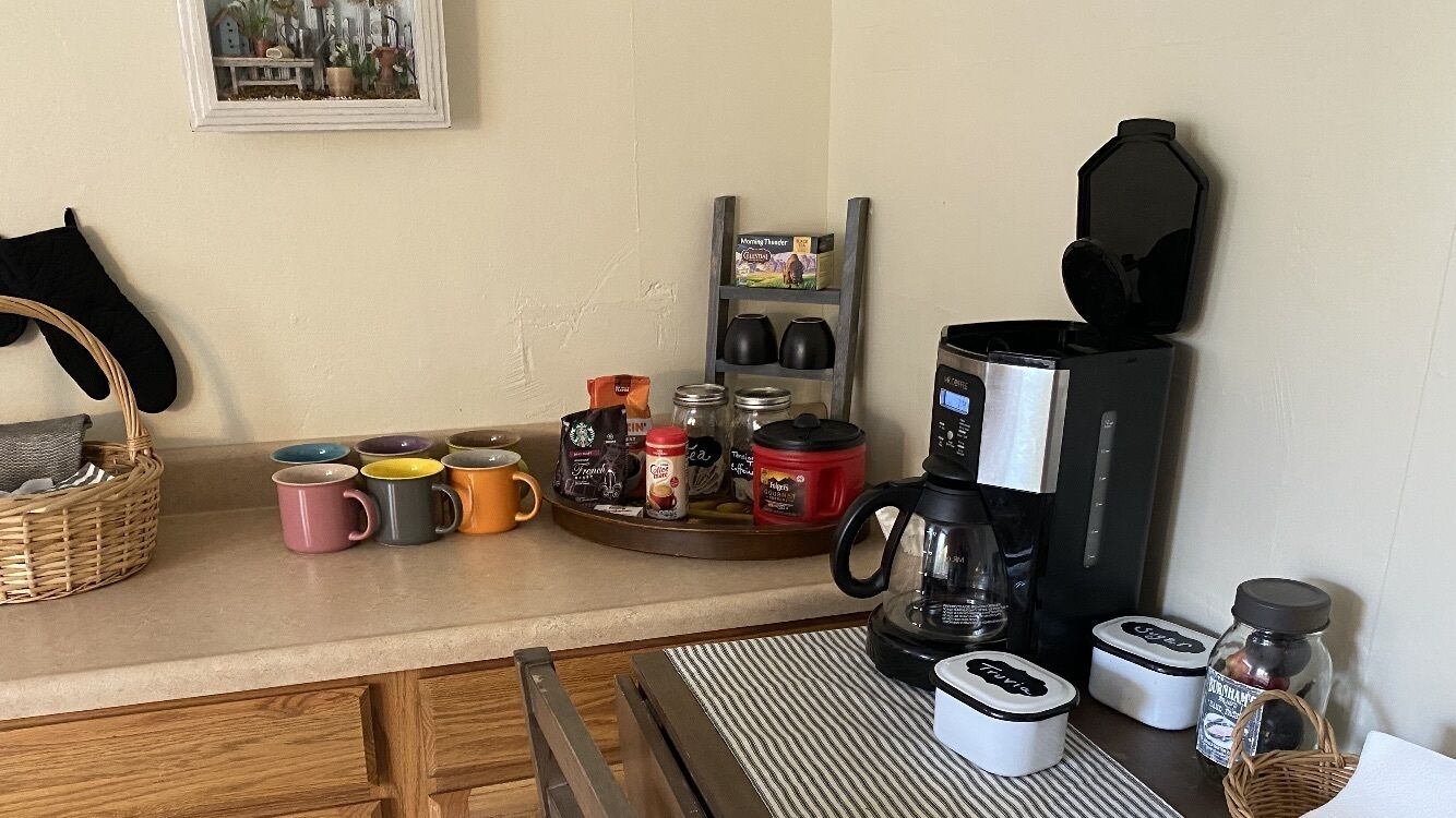 A kitchen counter with a coffee maker, mugs, jars, and a shelf with kitchenware.