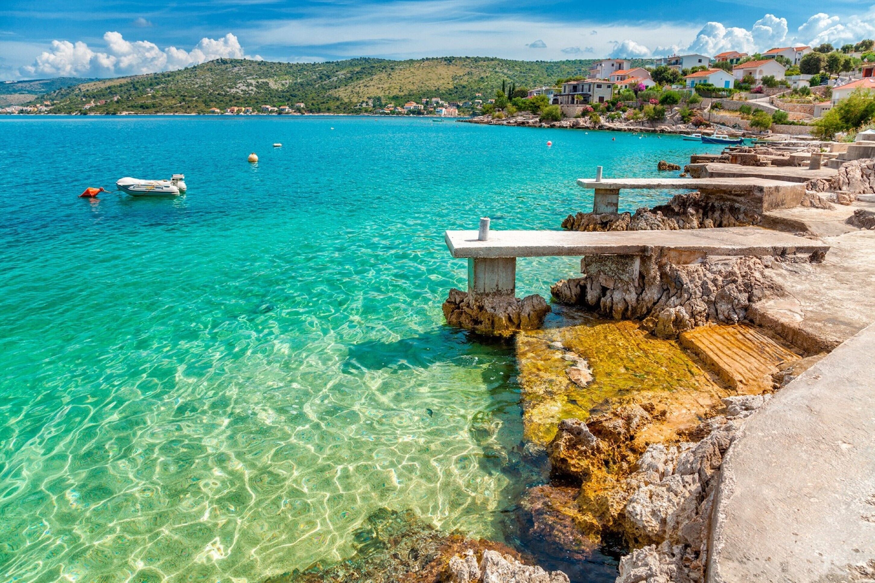 A coastal scene with clear turquoise water, rocky shore, and a small boat.