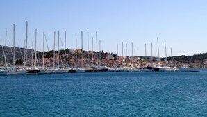 A marina with multiple sailboats docked, a coastal town in the background, and clear skies.