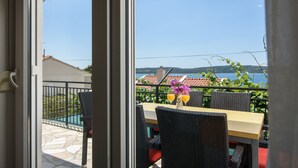 A terrace with a table and chairs, a view of the sea, and a pool in the background. - A3-90m2 apt w shared pool & balcony,next to beach (Trogir)