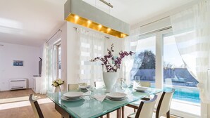A modern dining area with a glass table, white chairs, and a vase of flowers. - Beautiful Villa with swimming-pool in Pula Croatia (Pula)