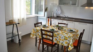 Een keuken met witte kasten, een roestvrijstalen spoelbak en een eettafel met een tafelkleed met citroenmotief.