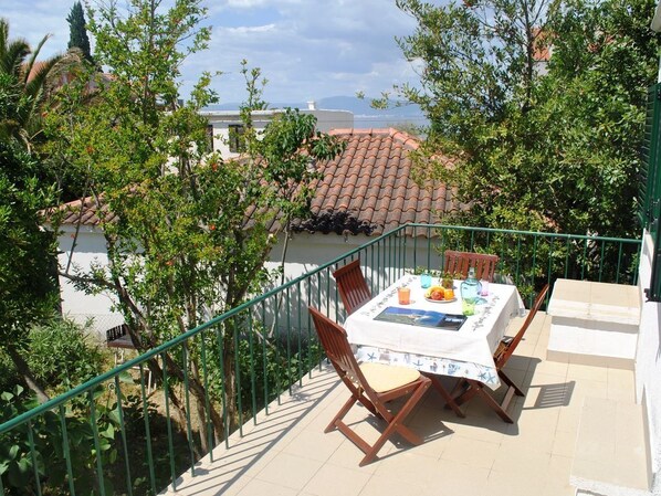 A terrace with a table set for two, surrounded by greenery and overlooking a cityscape.