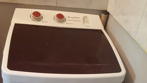 A front-loading washing machine with a control panel, a label on the door, and a power outlet on the wall. - Summer hill air bnb home away from home (St Ann)